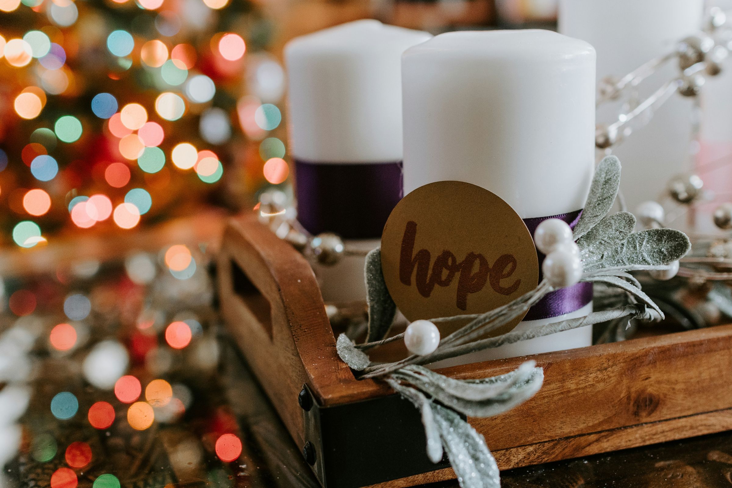 White pillar candle with "hope" message and colored Christmas lights in the background