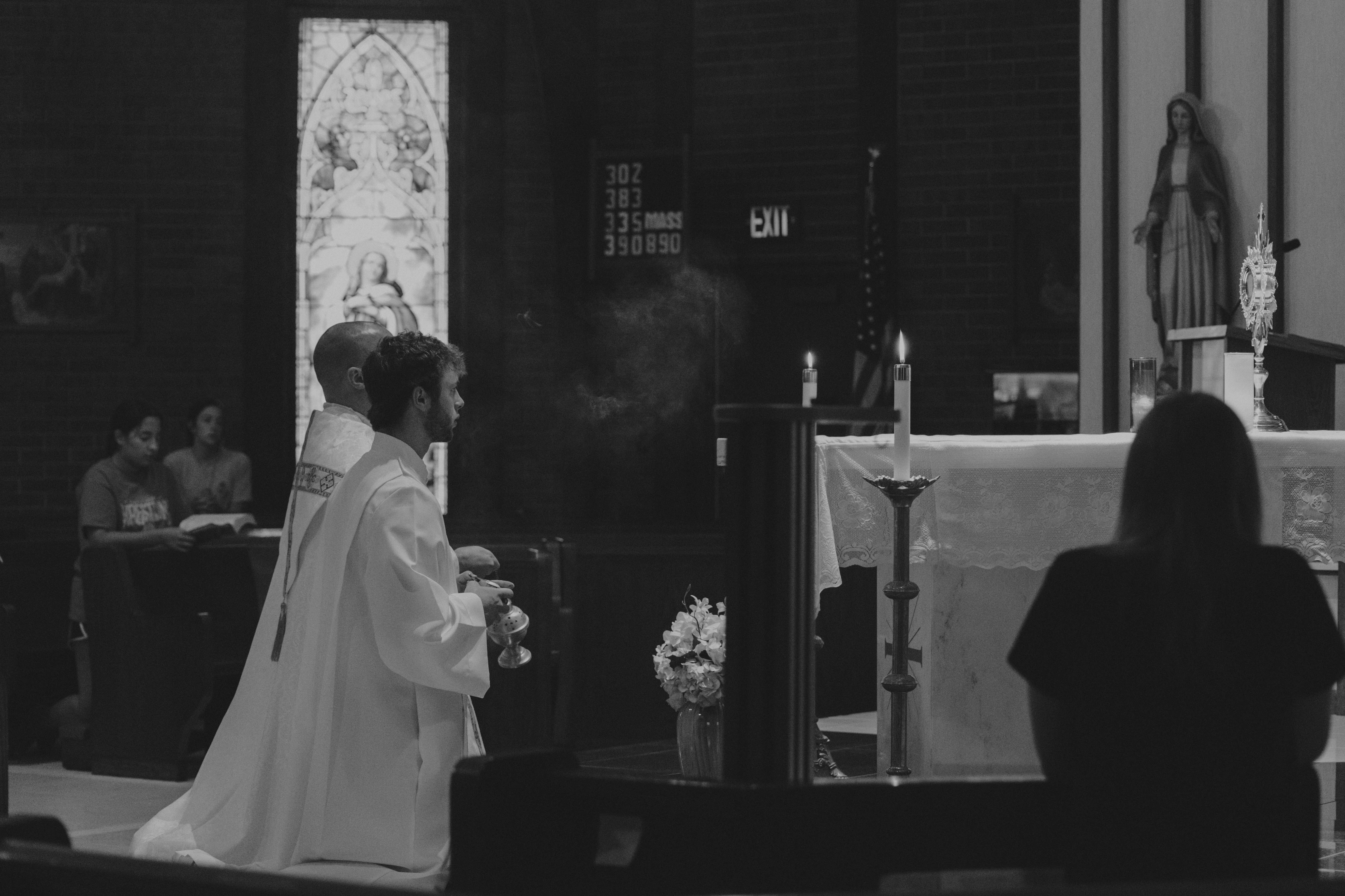 Black and white photo of a priest and altar server kneeling before the Eucharist during adoration