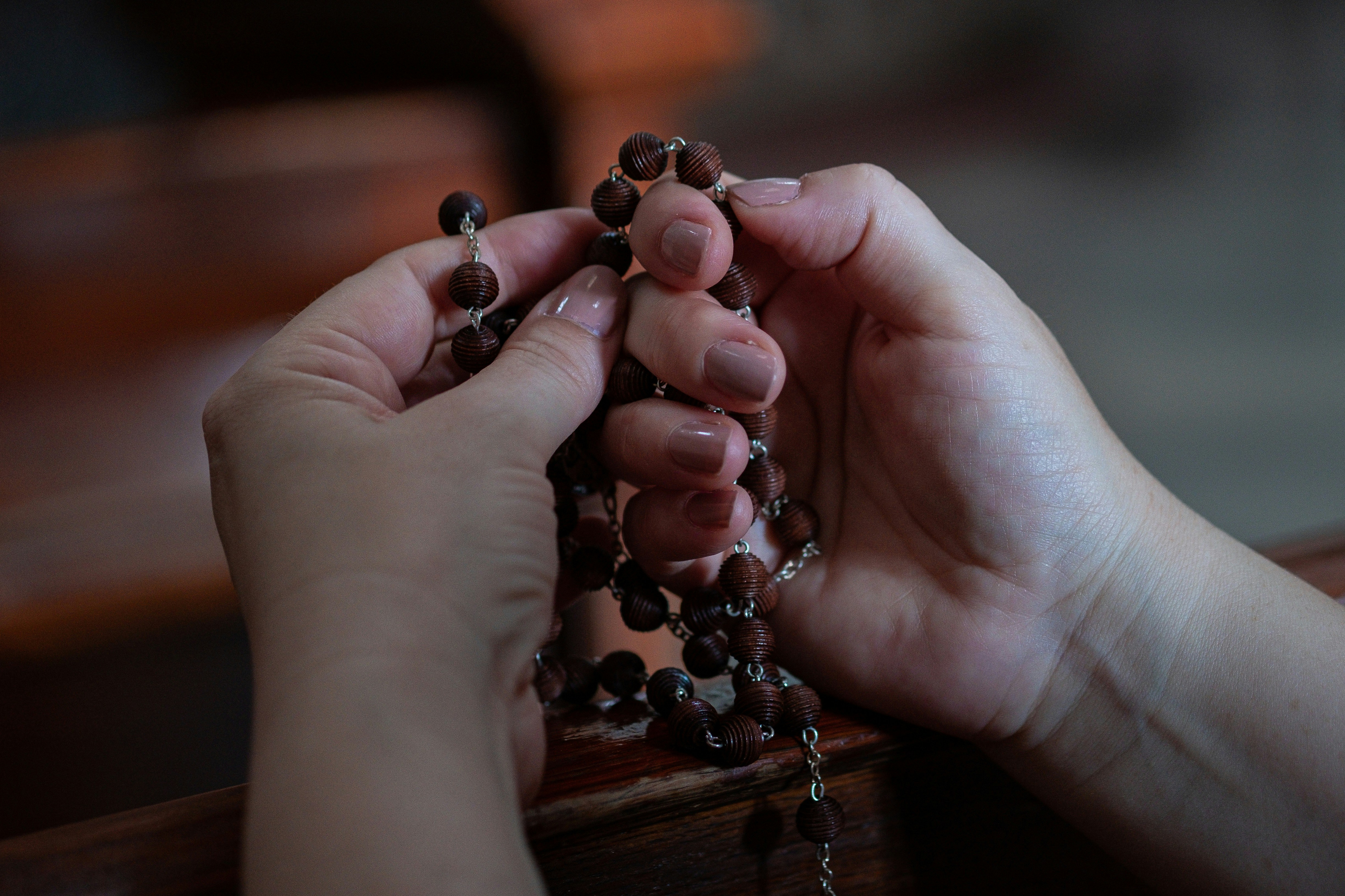 Close-up image of a woman's hands holding wooden Rosary beads