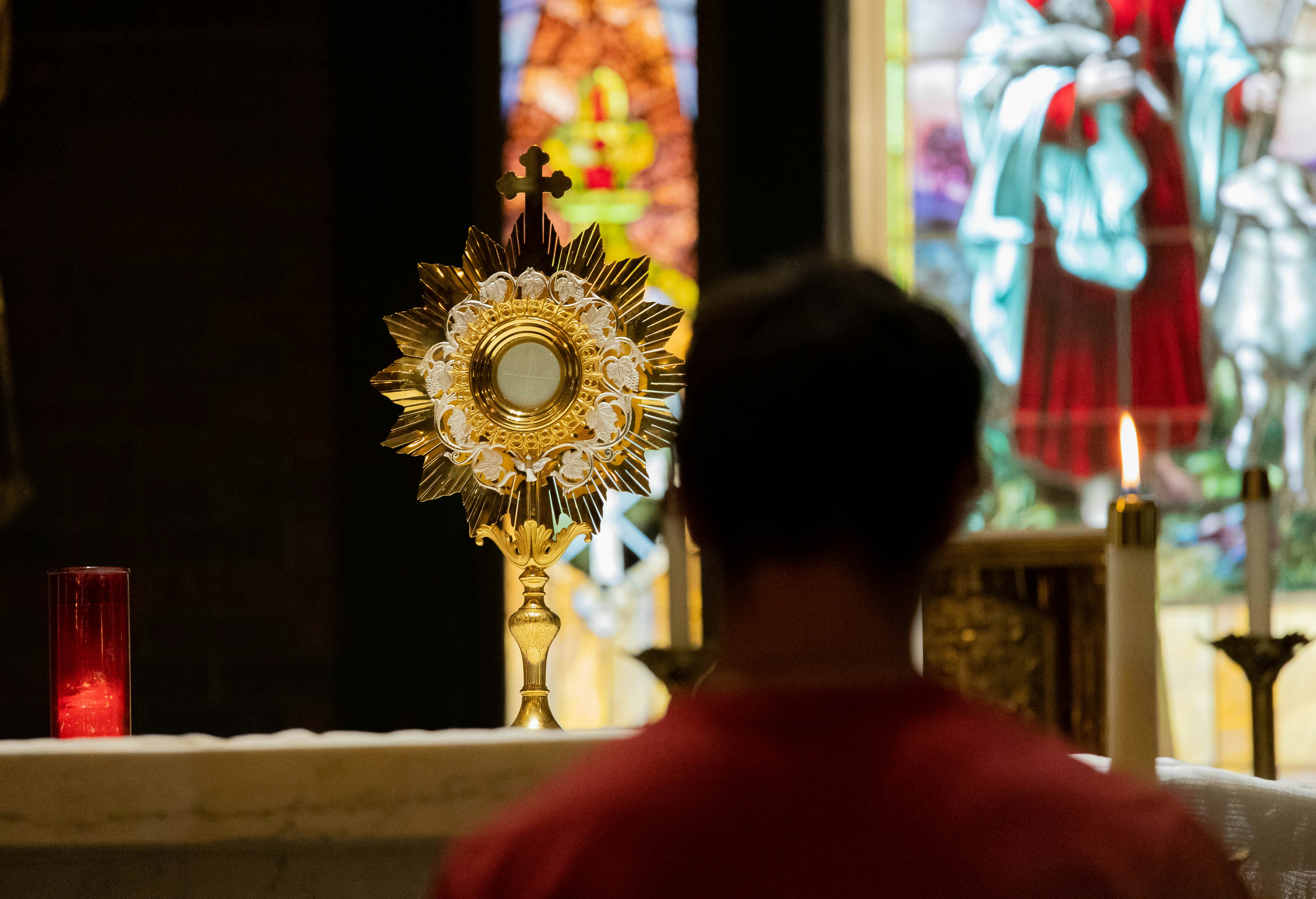 Young man sitting in front of the Eucharist during adoration with stained glass in the background