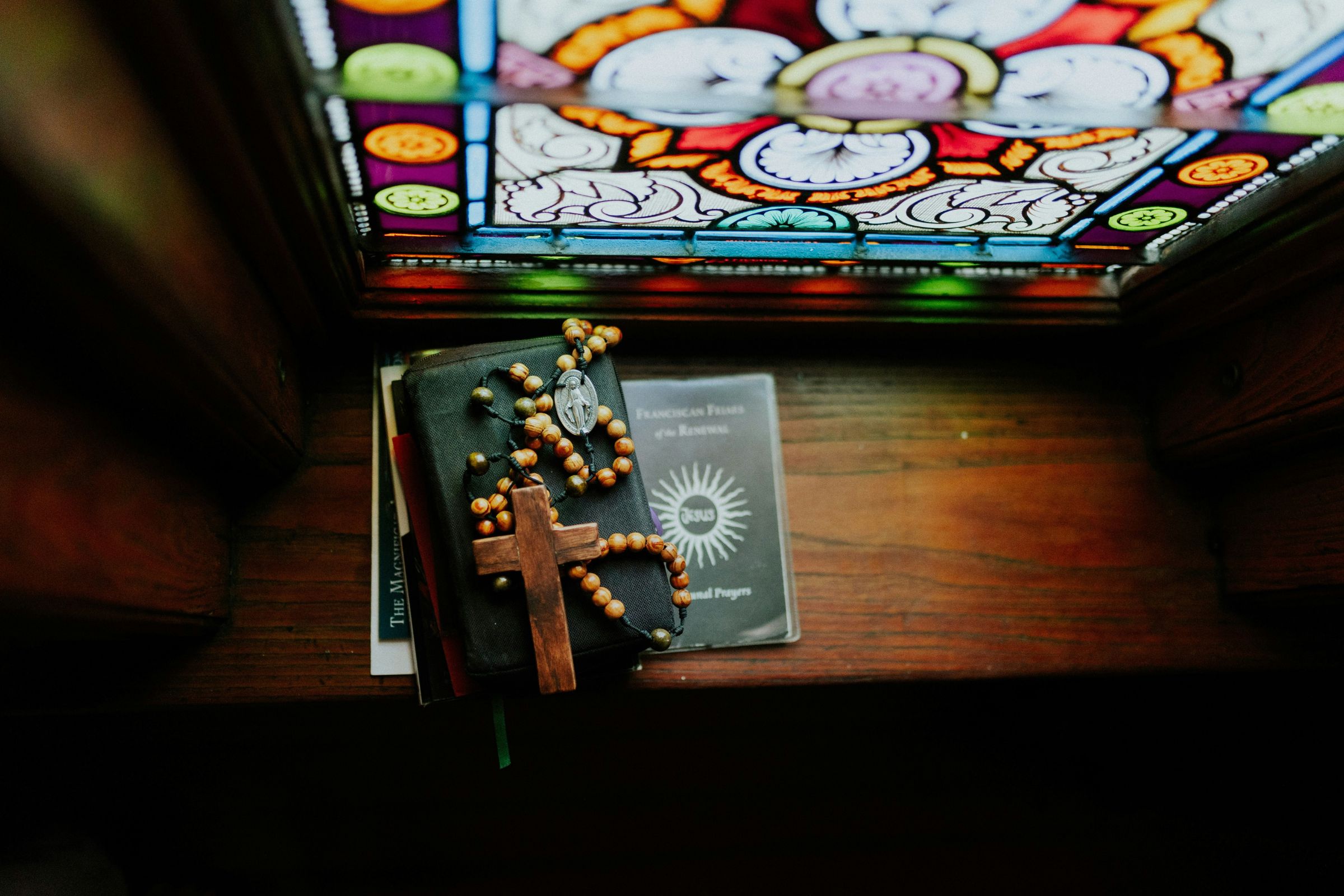 Rosary beads and prayer books on a window ledge below a stained glass window
