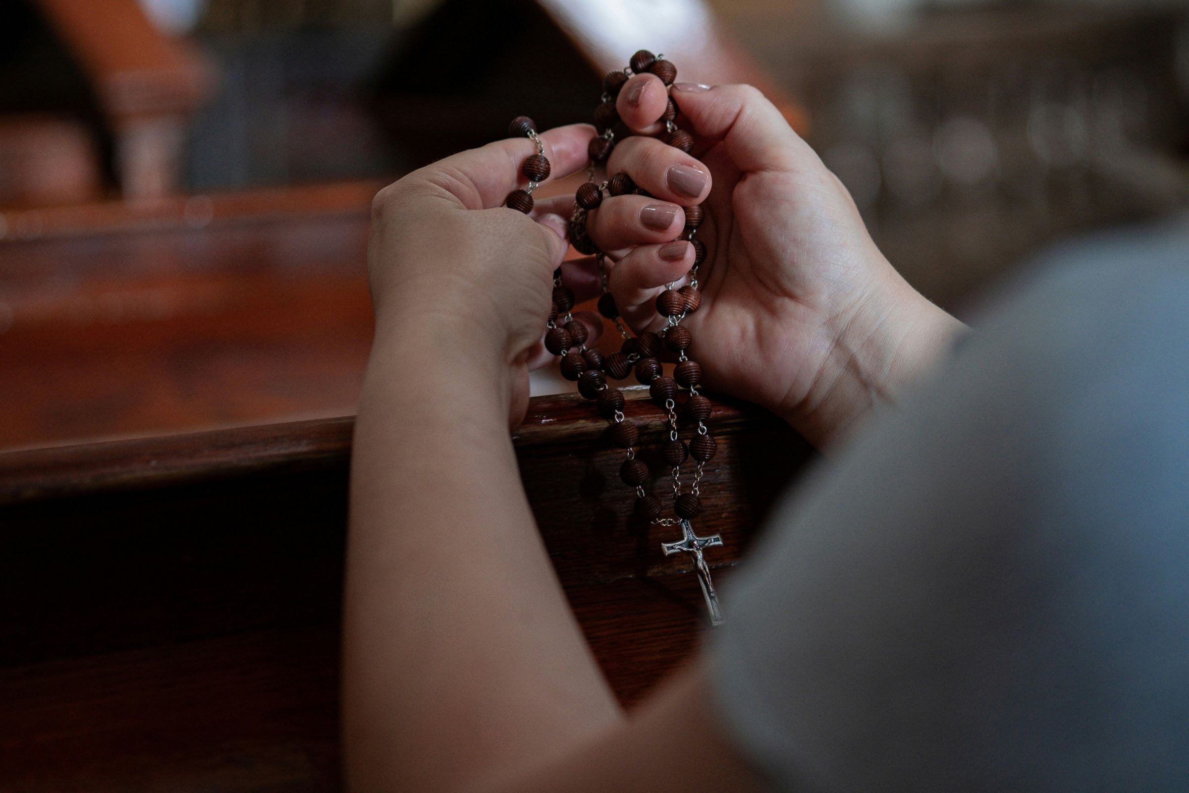 Close-up of young woman kneeling in a pew holding rosary beads